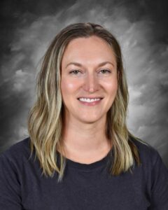 Smiling woman with long, wavy blonde hair, wearing a black shirt, against a gray background.