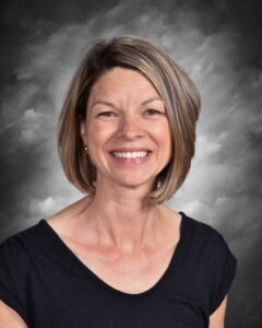A smiling woman with short, layered hair wearing a black shirt, set against a gray background.