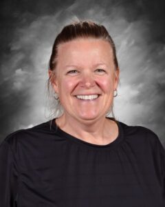 Smiling woman with shoulder-length hair, wearing a black shirt, against a gray background.