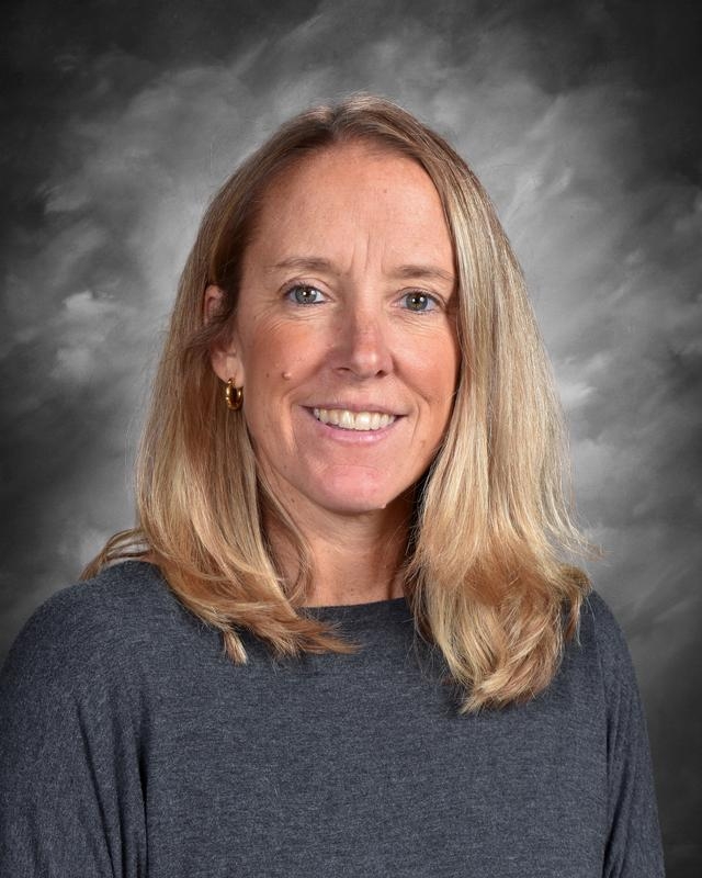 Smiling woman with long blonde hair, wearing a gray sweater, against a soft gray background.