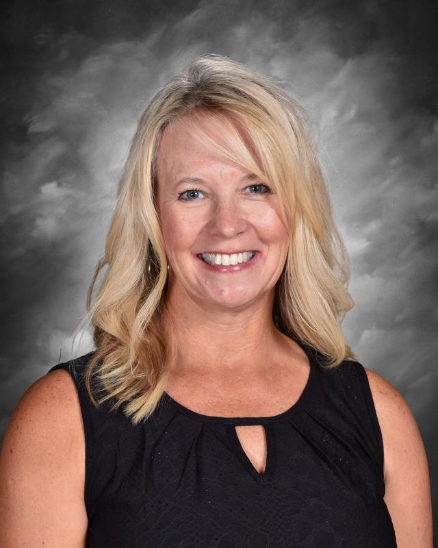 Smiling woman with blonde hair, wearing a black top, against a gray background.