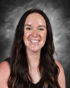 Smiling woman with long dark hair, wearing a black top, against a gray background.