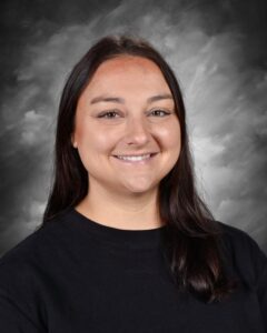 Smiling woman with long dark hair, wearing a black shirt, against a gray background.