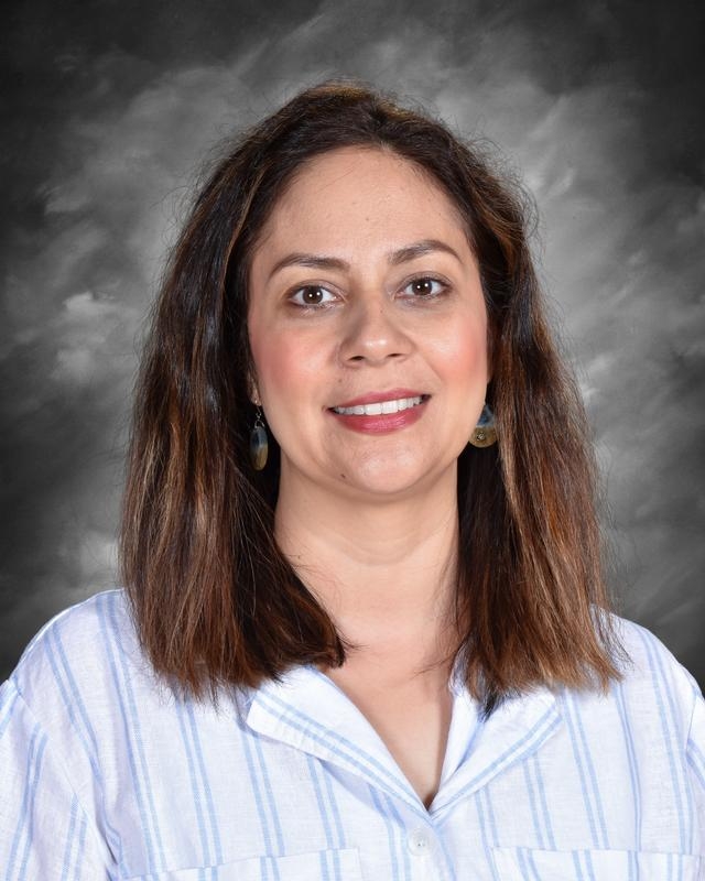 A woman with shoulder-length brown hair smiles, wearing a striped shirt and earrings, against a gray background.